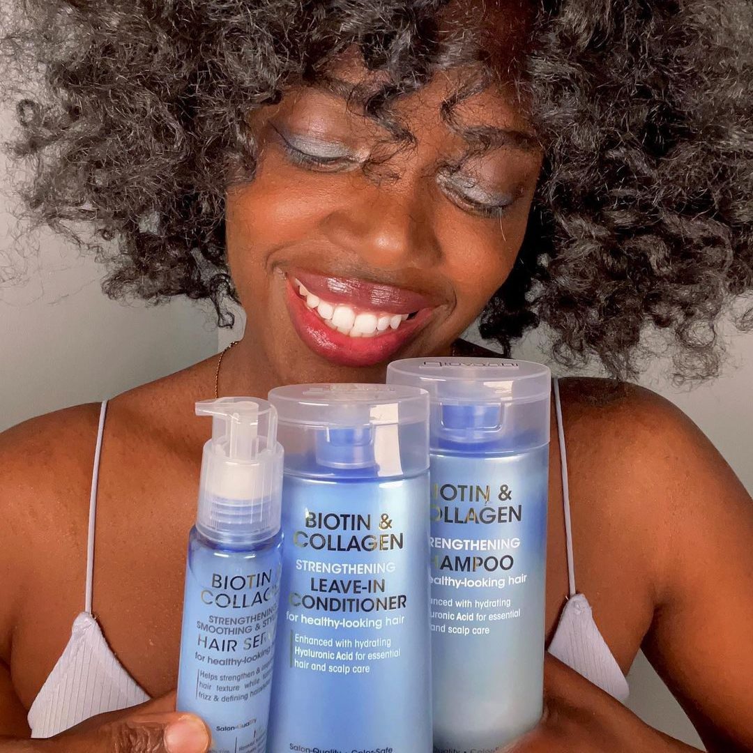 Femme souriante avec des produits capillaires en main, cheveux bouclés et peau lumineuse.