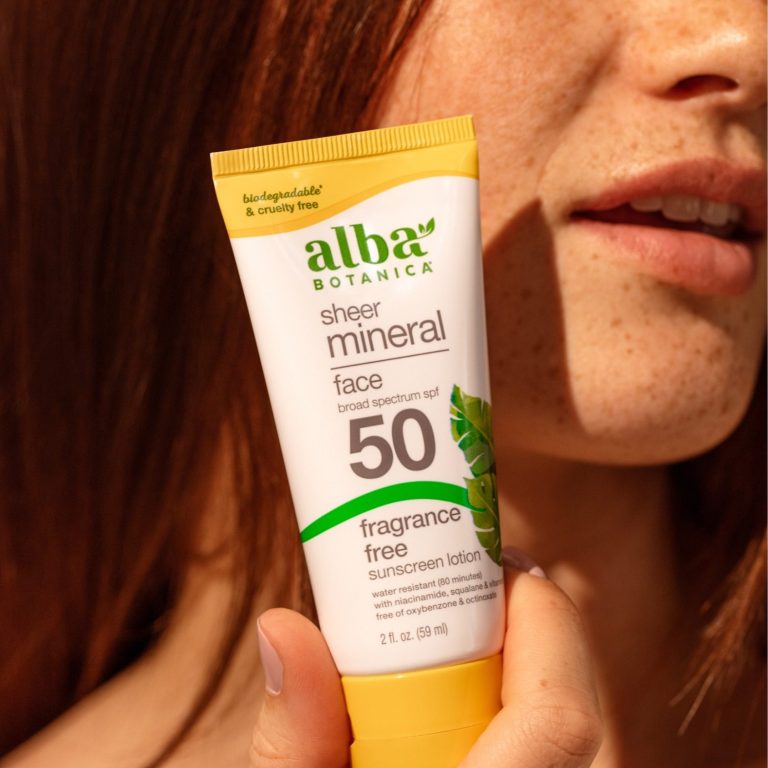 Crème solaire minérale FPS 50 sans parfum, tenue dans une main près du visage.