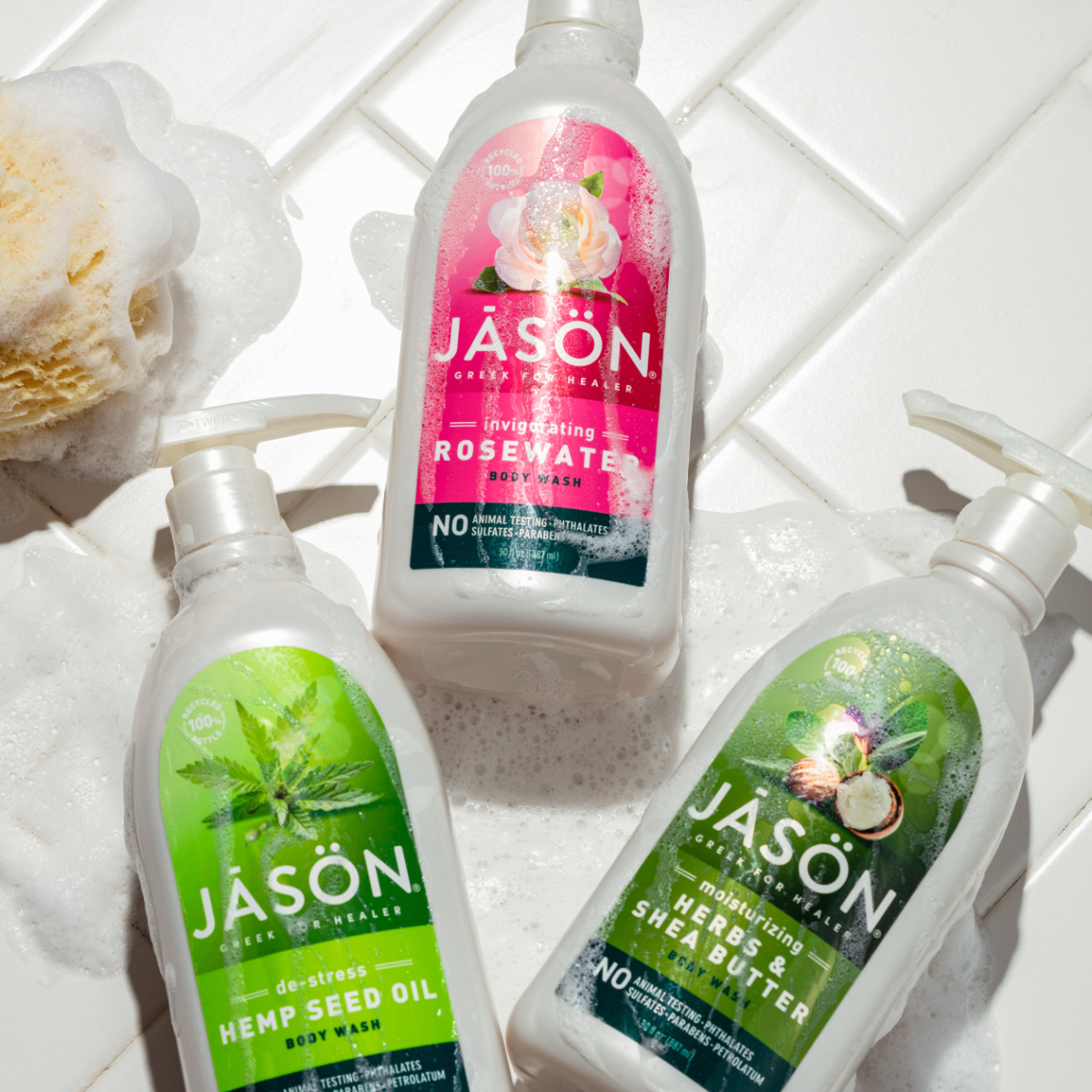 Trois bouteilles de shampooing Jason sur un carrelage, avec une éponge à côté.