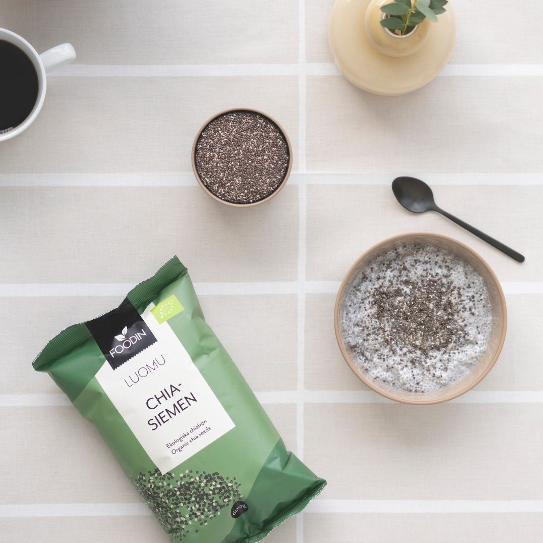 Paquet de graines de chia bio, bols avec graines, tasse de café et plante en pot sur table claire. Paquet de graines de chia bio, bols avec graines, tasse de café et plante en pot sur table claire.