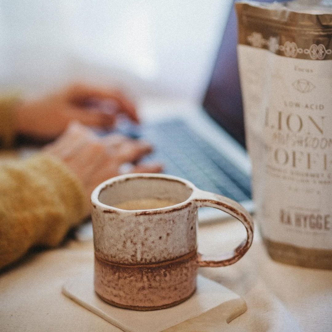 Une tasse de café champignon bio sur une table près d'un ordinateur portable et un paquet de café bio champignon 
