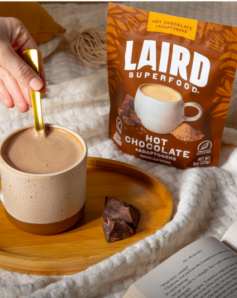 Tasse de chocolat chaud sur une assiette avec un sachet de poudre et un livre à côté.
