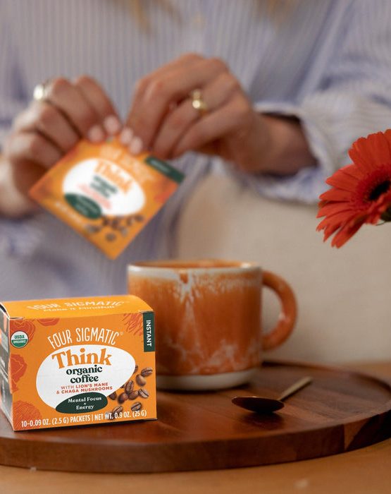 Person verse un sachet de café bio Think dans une tasse orange sur une table en bois.