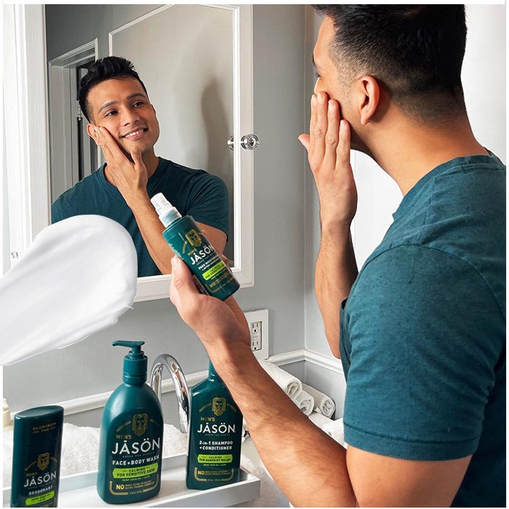 Homme souriant se nettoyant le visage devant un miroir avec des produits de soin.Jason bion homme