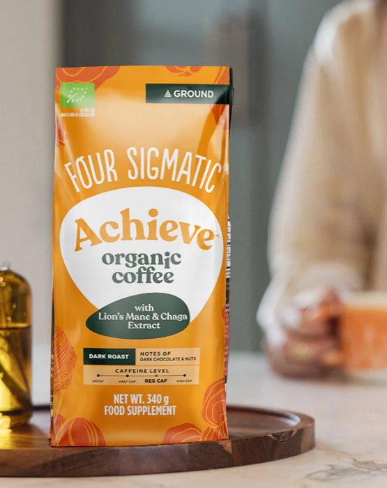 Paquet de café bio "Achieve" de Four Sigmatic sur une surface claire, avec une tasse à côté.