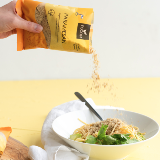 ParaVEGANO est une râpe végétalienne Main d'une personne saupoudrant du parmesan sur une salade dans un bol blanc.
