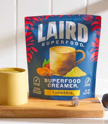 Sachet de crémer superaliment au curcuma avec tasse et cuillère en bois.